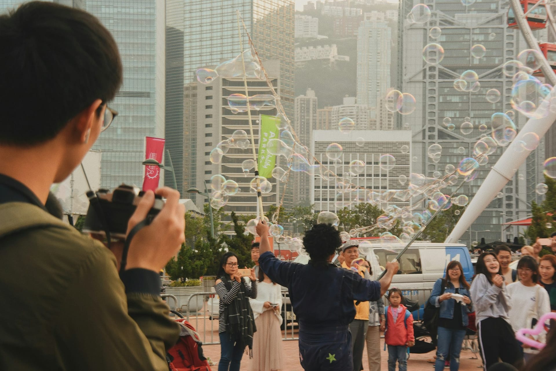 Artista de rua soprando bolhas de sabão gigantes no distrito Central de Hong Kong com arranha-céus sobre Victoria Harbour.