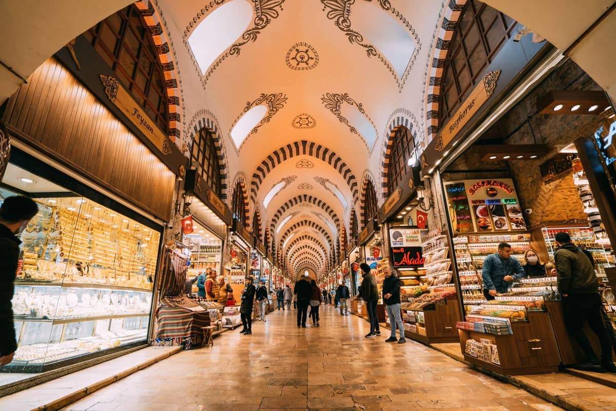 Vue large du Grand Bazar animé d'Istanbul avec son plafond voûté, ses boutiques éclairées, ses vitrines de bijoux et ses acheteurs déambulant dans un large couloir.