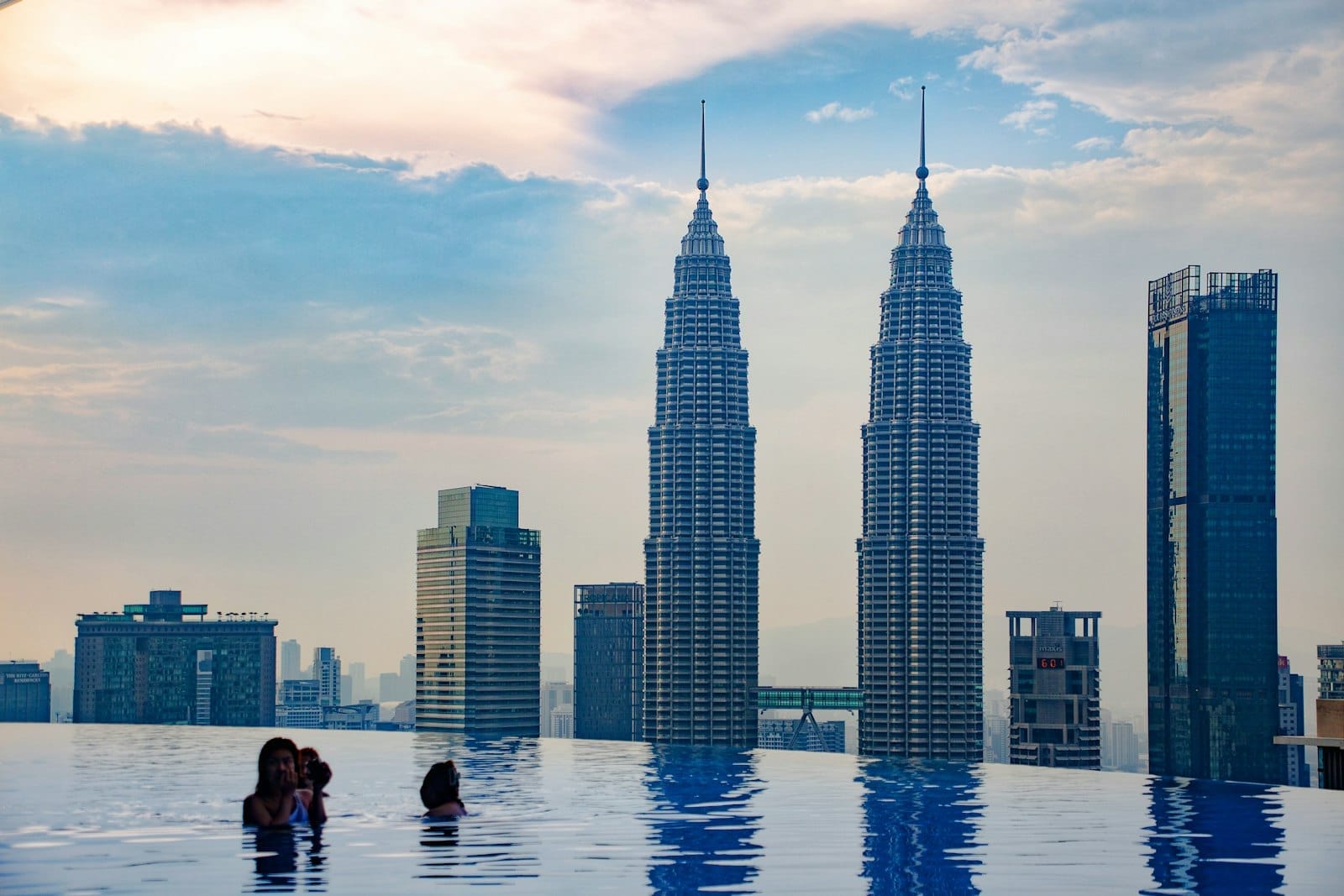 Infinity pool with people enjoying the view of Kuala Lumpur skyline, featuring the Petronas Twin Towers at sunset.