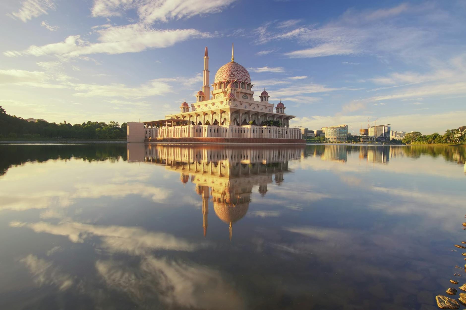 The pink-domed Putra Mosque stands beside a calm lake in Kuala Lumpur, with its detailed reflection mirrored in the water.