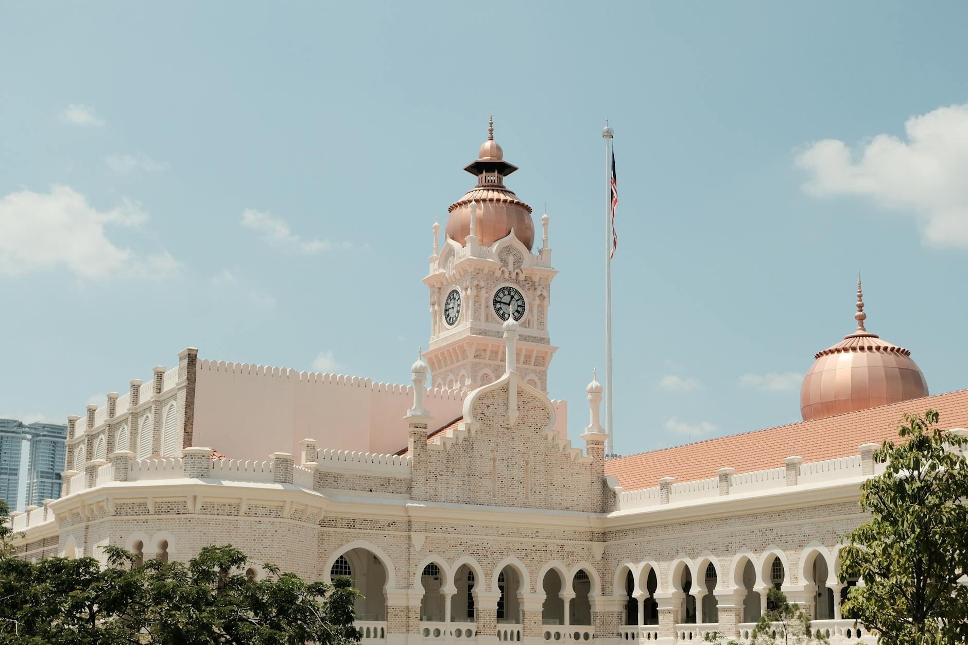 Sultan Abdul Samad Building in Kuala Lumpur featuring a copper dome and clock tower under clear blue skies with soft sunlight.