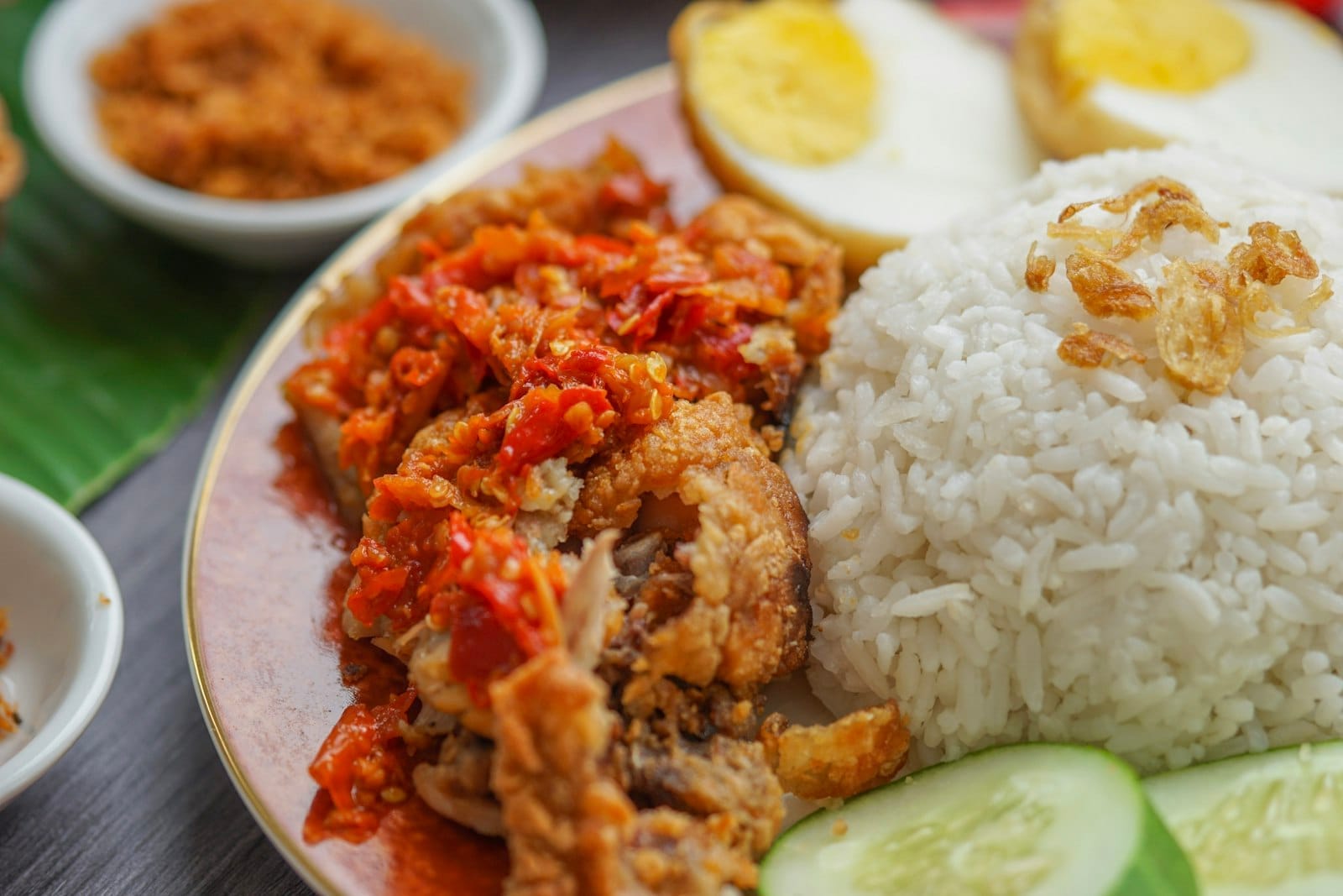 A traveler's plate of nasi lemak in Kuala Lumpur, highlighting local cuisine with spicy chicken, rice, egg and cucumber ready to be enjoyed.