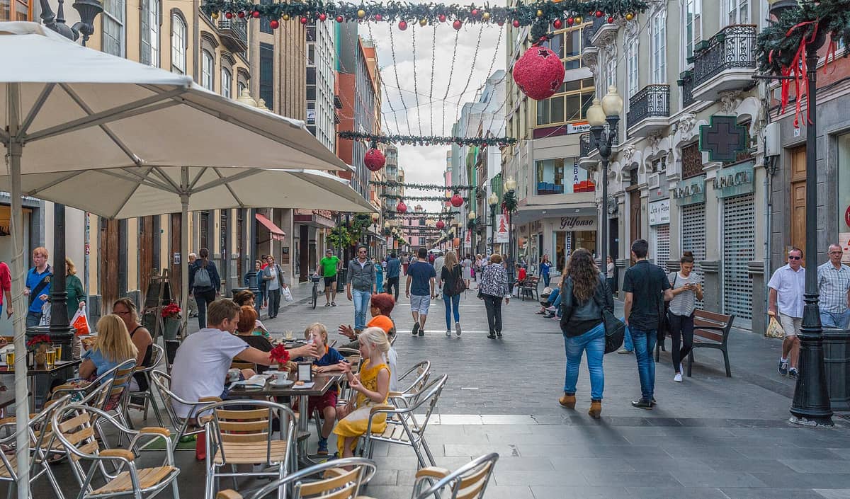 Пешеходная улица Calle Mayor de Triana в Лас-Пальмасе, оживлённая прохожими и посетителями уличных кафе, украшенная праздничными огнями.