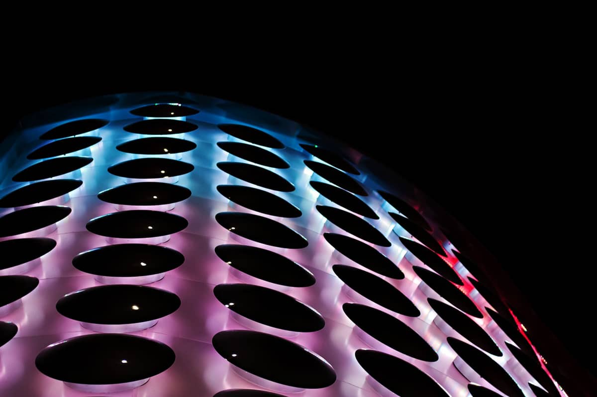 Gros plan d'une structure de dôme futuriste éclairée avec des lumières LED colorées en rouge, violet et bleu sur un ciel nocturne noir.