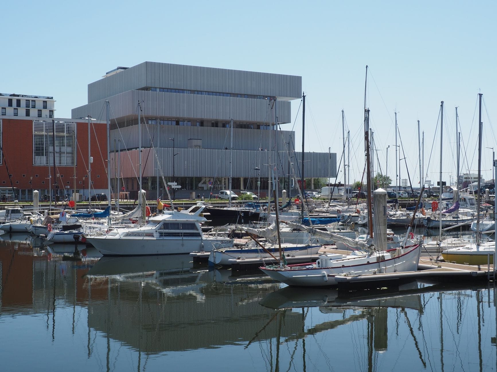 Barche moderne ormeggiate nel porto di Le Havre con la caratteristica architettura del Museo MuMa sullo sfondo in una giornata serena.
