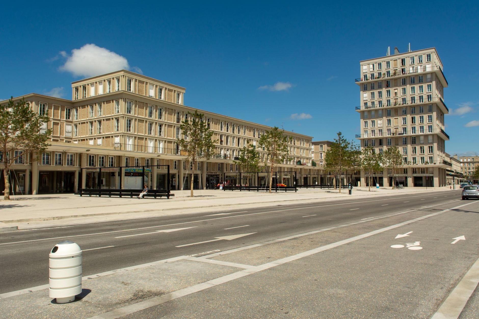 Szeroki widok na centrum miasta Le Havre zaprojektowane przez Perreta, z modernistycznymi modułowymi budynkami betonowymi i wyraźnym układem siatki ulic, pod jasnym błękitnym niebem.