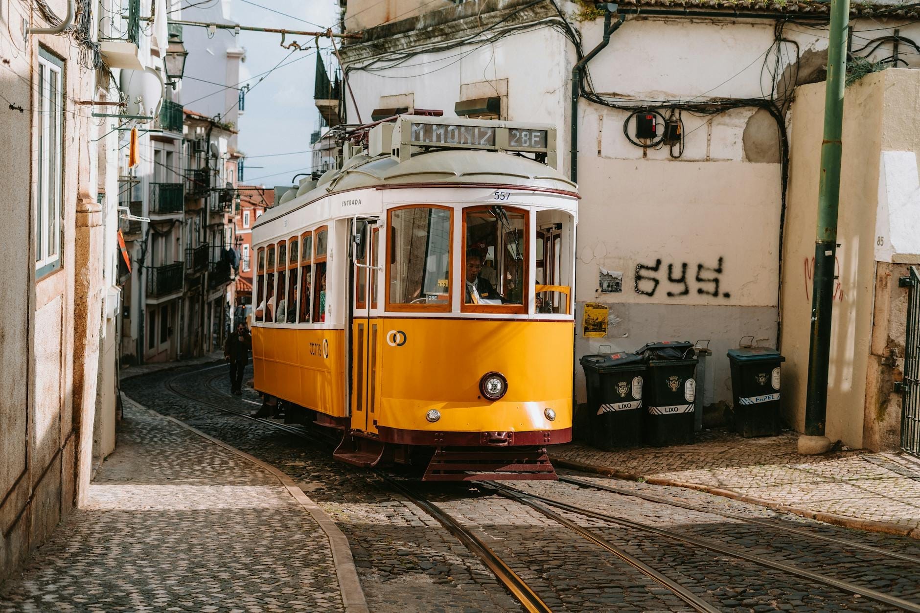 Un tramway jaune classique de Lisbonne traverse une rue étroite, pavée et escarpée, bordée de vieux bâtiments à Alfama ou Graça.