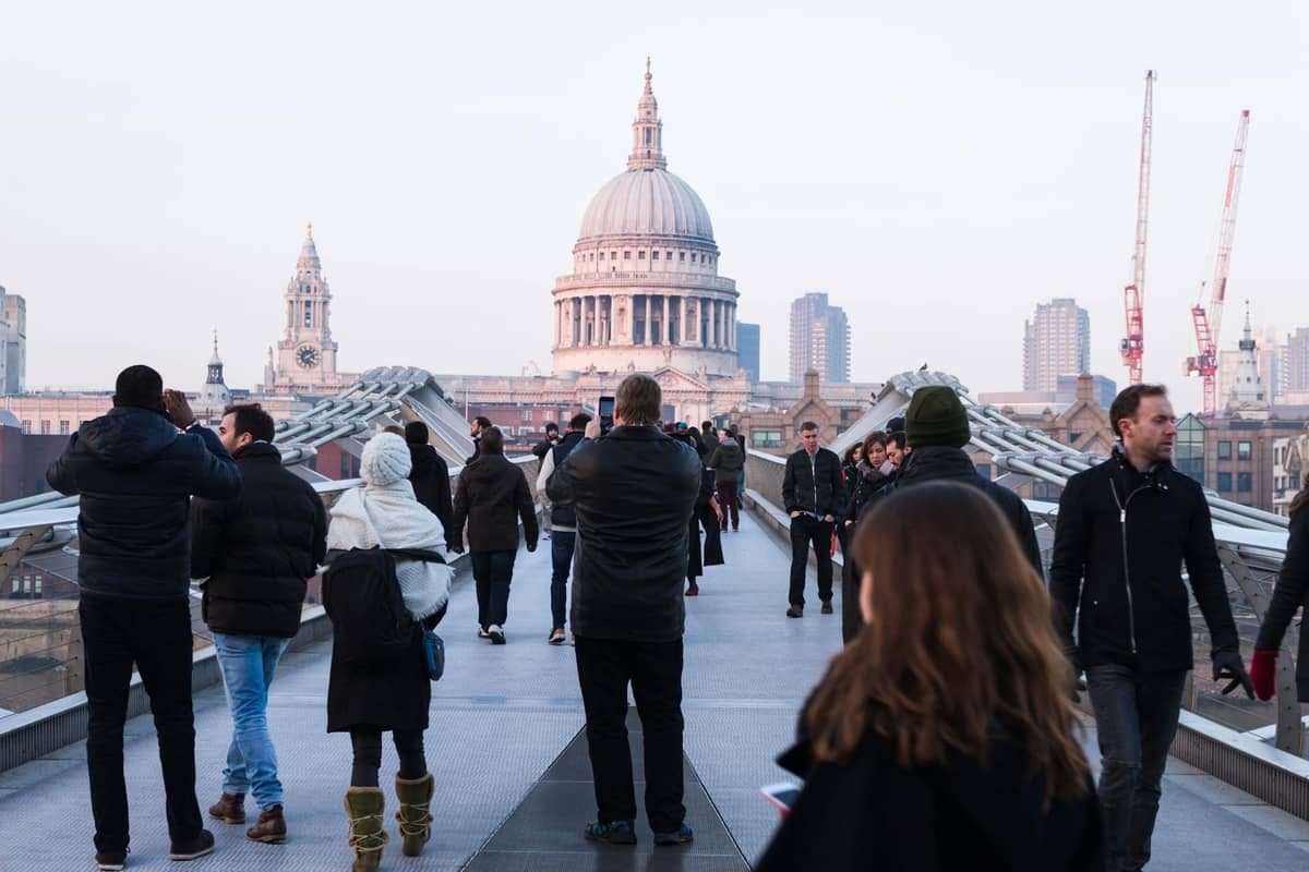 Pessoas caminhando pela Millennium Bridge com a Catedral de St Paul's e o centro de Londres visíveis ao fundo.