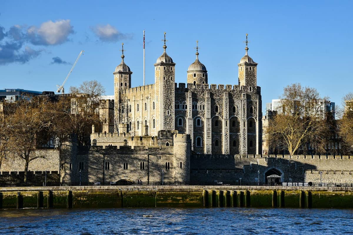 A Torre de Londres com suas históricas muralhas de pedra e torres, vista do outro lado do rio Tâmisa em um dia claro.