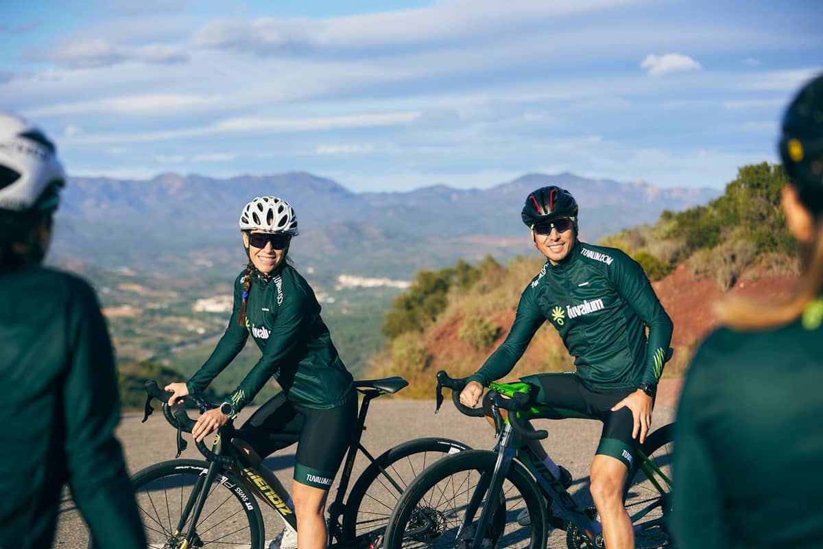 Cyclists in professional gear riding on a scenic mountain road with Mallorca's Tramuntana mountains in the background.