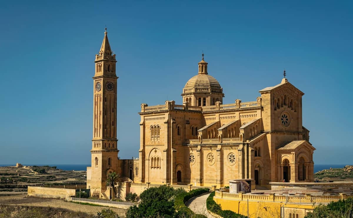 Große historische Kirche mit einem hohen Glockenturm auf der Insel Gozo, Malta, in Sonnenlicht getaucht unter einem klaren blauen Himmel.