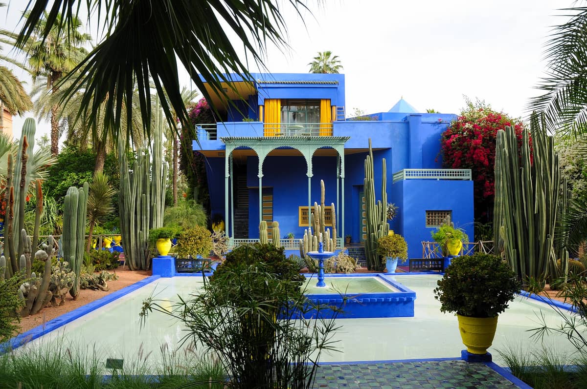 สวน Majorelle อันโด่งดังในเมือง Marrakech พร้อมวิลล่าสีฟ้าโคบอลต์ที่โดดเด่น ต้นกระบองเพชร ต้นปาล์ม และน้ำพุที่ล้อมรอบด้วยพืชพรรณสีเขียวอุดมสมบูรณ์
