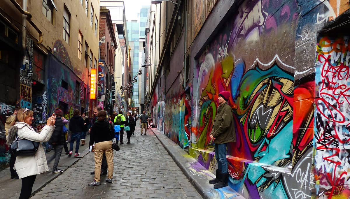 Menschen, die Fotos machen und durch eine farbenfrohe Gasse in Melbourne spazieren, die mit lebhaften Street-Art-Murals und Graffiti bedeckt ist.