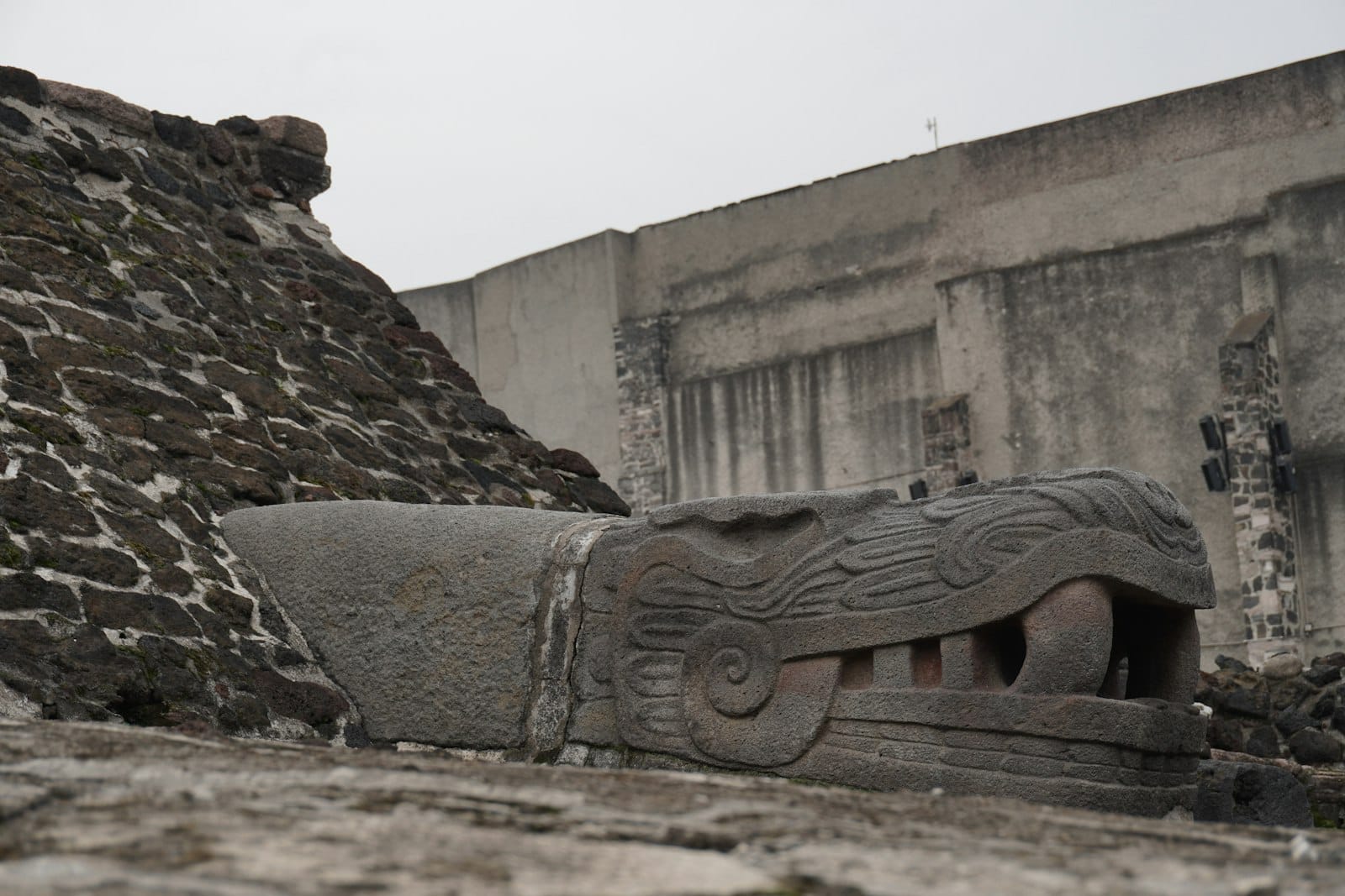 Close-up de uma escultura de cabeça de serpente em pedra entre antigas ruínas de pedra em um sítio arqueológico pré-hispânico no centro da Cidade do México.