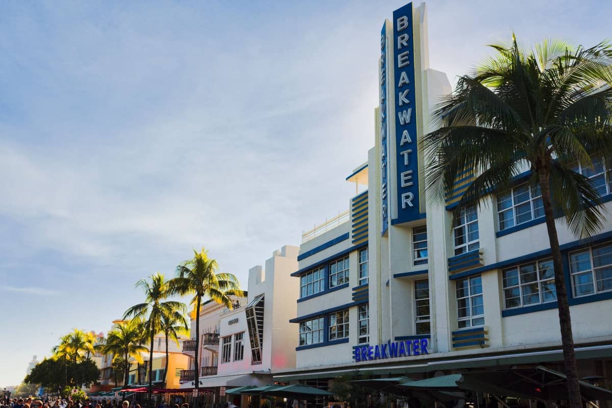 Daytime view of Miami's Ocean Drive featuring classic Art Deco hotels with palm trees and blue sky, iconic of the Art Deco Historic District.