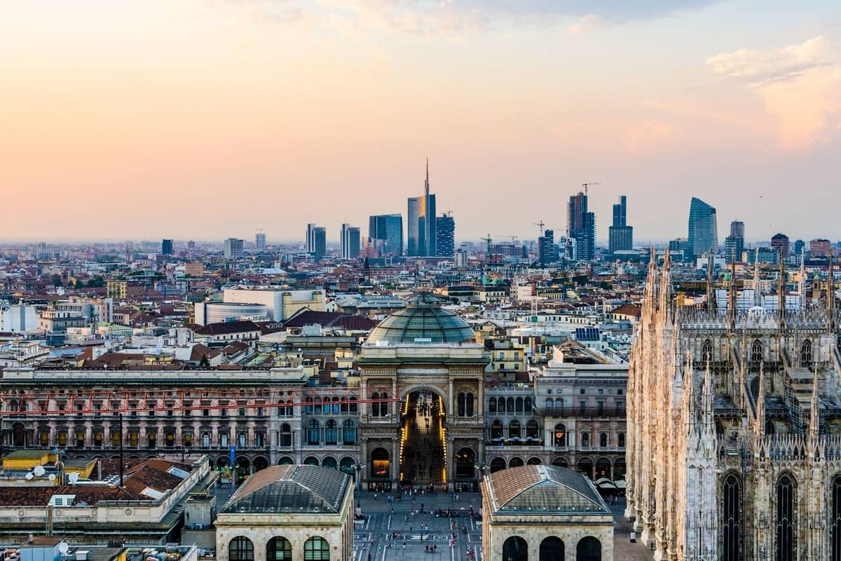 Vista aérea ampla de Milão com o Duomo, a Galleria Vittorio Emanuele II e arranha-céus modernos ao pôr do sol.