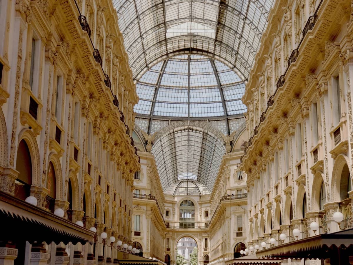 Vista interior ampla da Galleria Vittorio Emanuele II de Milão, mostrando seu ornamentado teto arqueado de vidro e sua elegante arquitetura histórica.