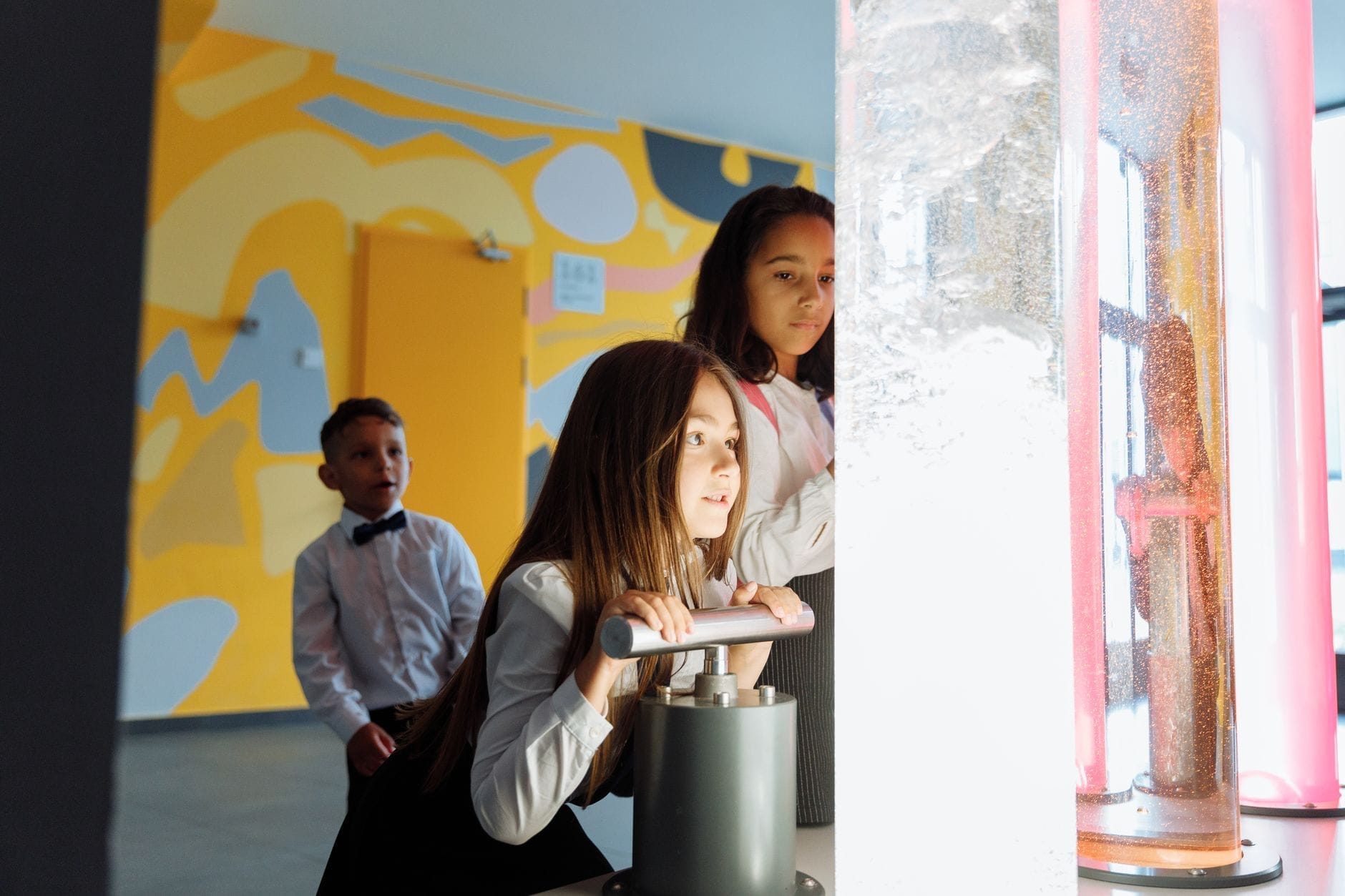 Niños interactúan con coloridas exposiciones científicas en un espacio interior con paredes de patrones amarillos, participando en actividades adecuadas para niños en Nashville.