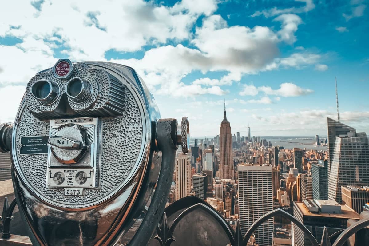 Klassischer münzbetriebener Aussichtsfernrohr mit Blick auf die Skyline von New York City mit dem Empire State Building und Wolkenkratzern, die an einem sonnigen Tag deutlich zu sehen sind.