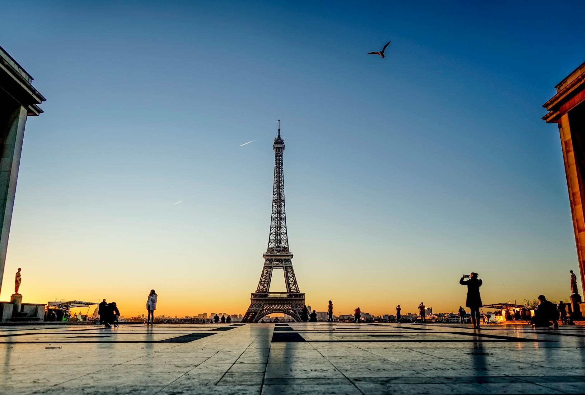 Blick auf den Eiffelturm bei Sonnenaufgang mit Silhouetten von Menschen und klarem Himmel, aufgenommen vom Trocadéro-Platz.