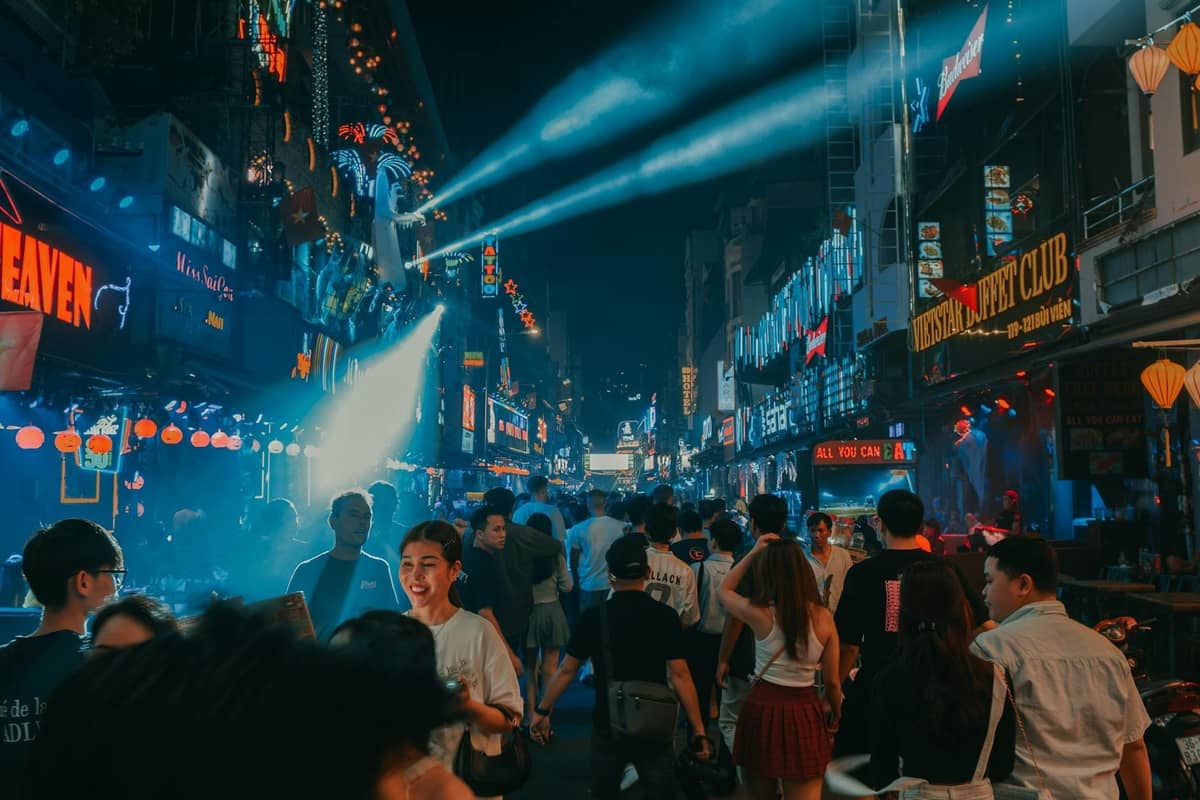 Bustling nightlife street scene with neon signs, crowds of people, bars, and clubs illuminated at night in an entertainment district.