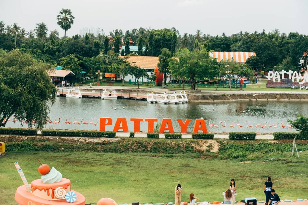Outdoor family attraction in Pattaya with a lake, colorful boats, large PATTAYA sign, greenery, and families enjoying the park.