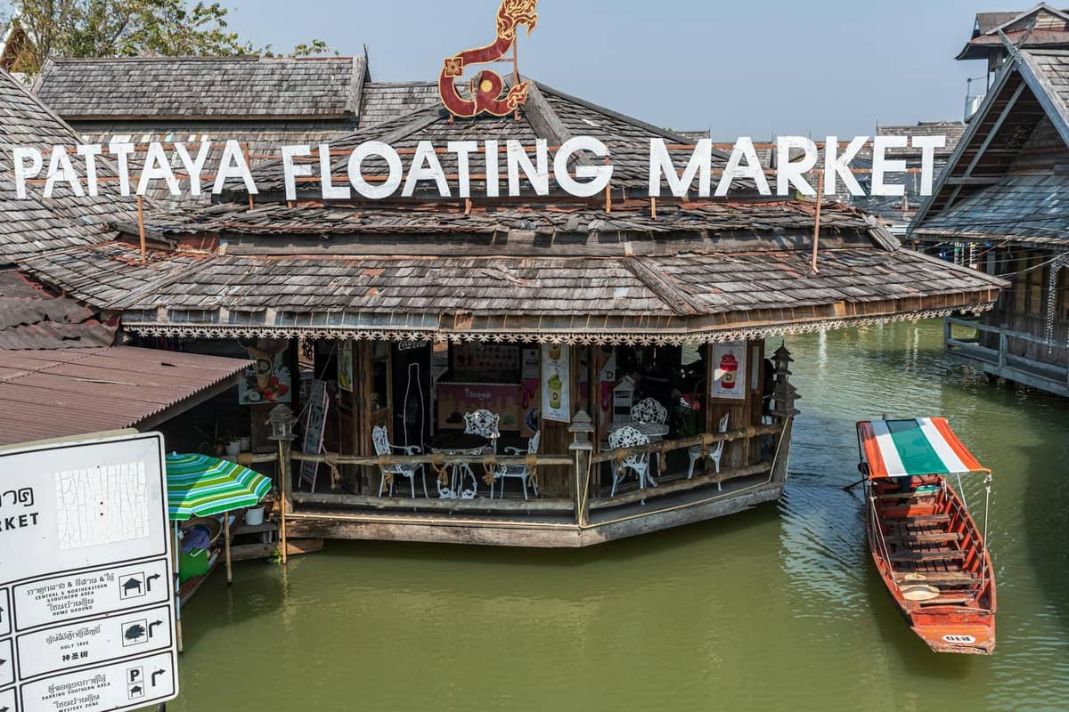 Pattaya Floating Market building with large sign over water, long-tail boat approaching, showcasing a famous shopping and food attraction in Pattaya.