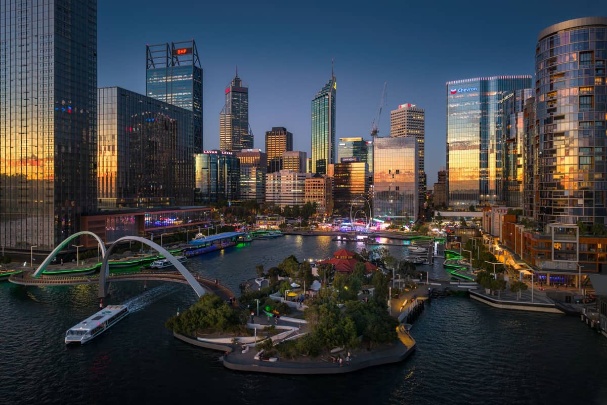 Abendlicher Blick auf Elizabeth Quay in Perth mit modernen Wolkenkratzern, Fußgängerbrücke, Uferpark und Booten unter einem Abendhimmel.