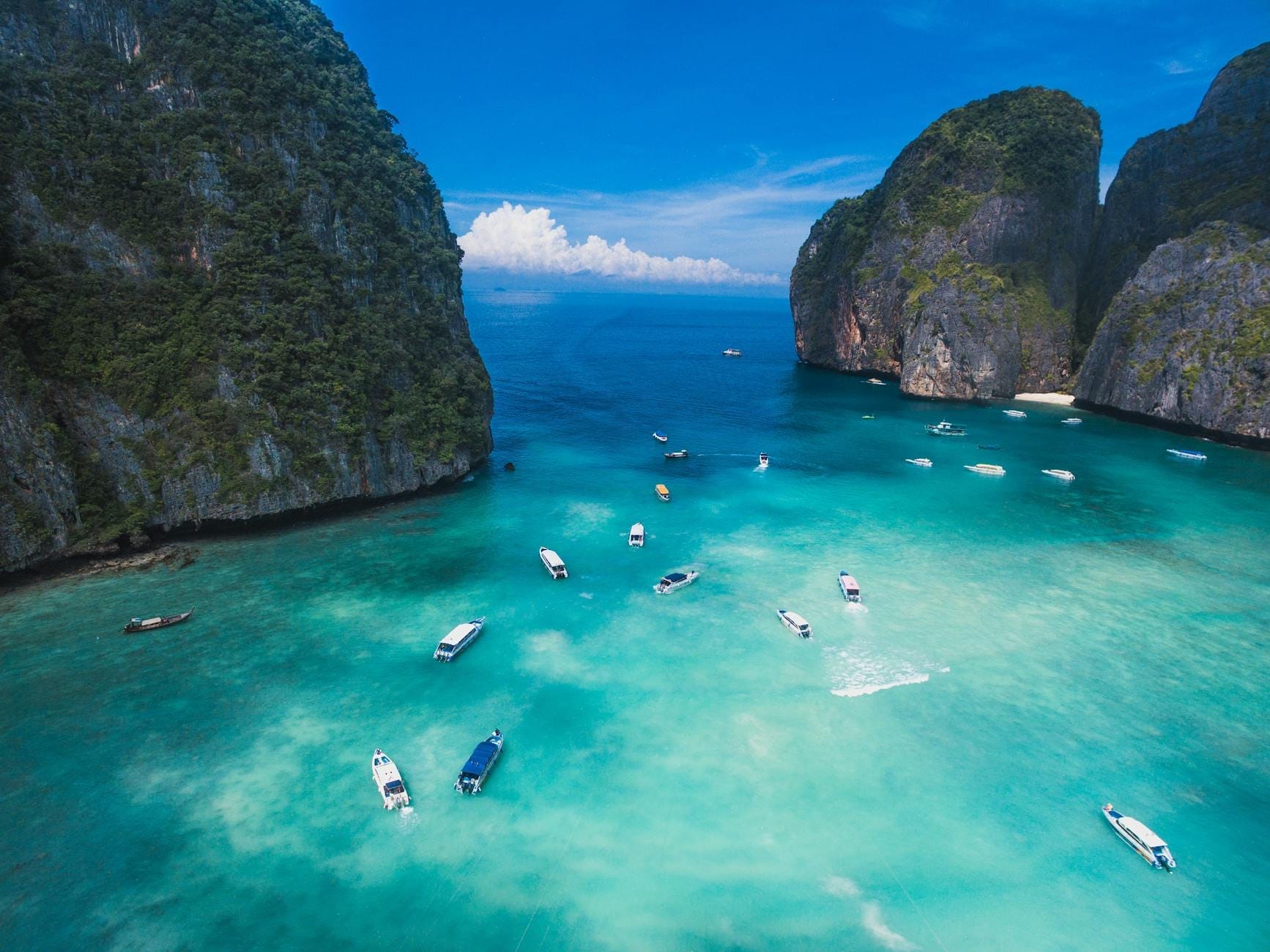Aerial view of turquoise water, speedboats, and dramatic limestone cliffs at a famous tropical bay near Phuket, Thailand.