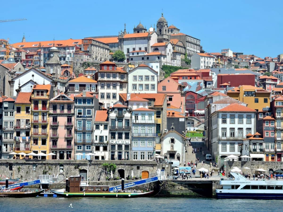 Colorati edifici storici lungo il fiume Douro nella città vecchia di Porto, patrimonio UNESCO, con barche e la cattedrale che si erge sullo sfondo.