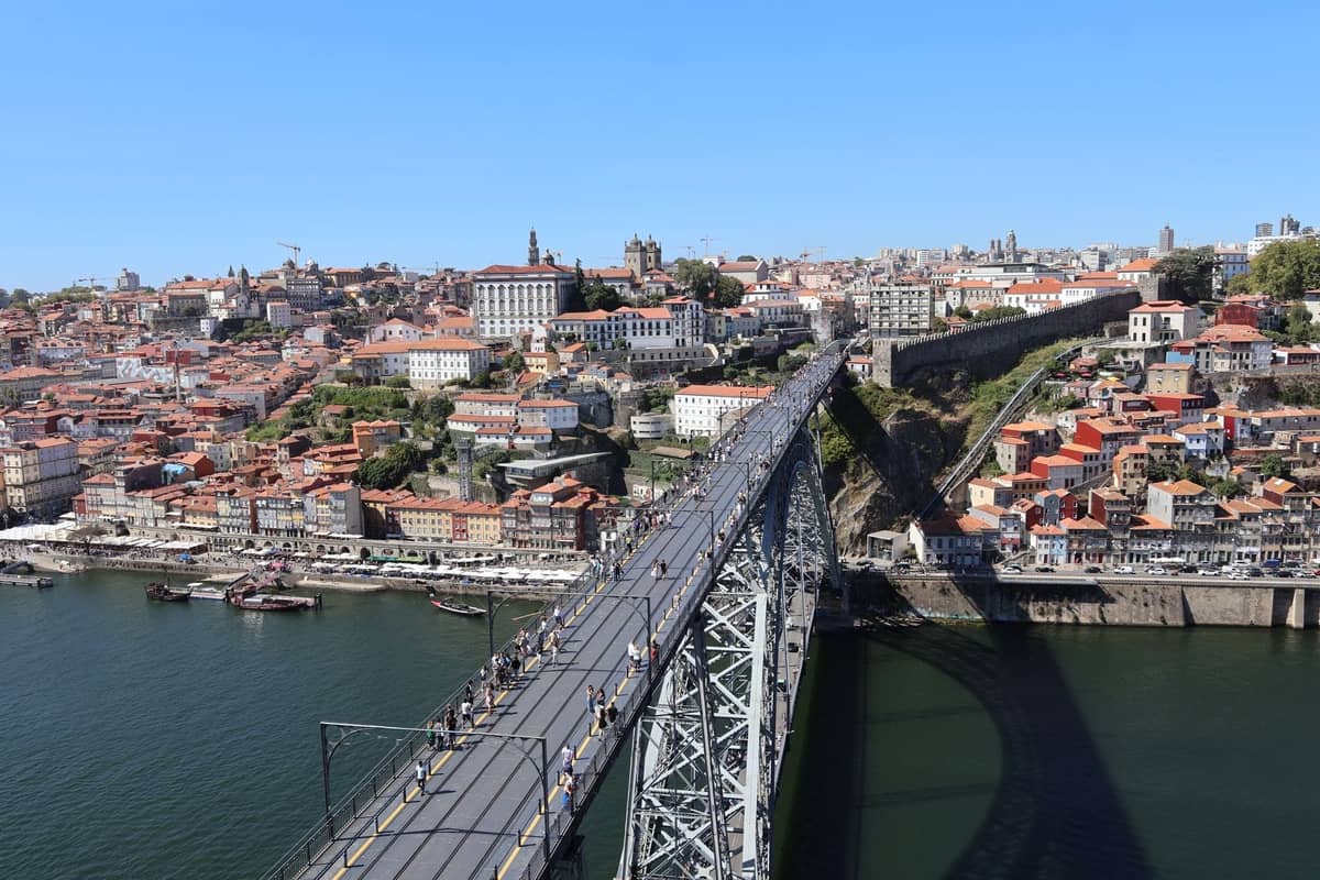 Vista dall'alto del Ponte Dom Luís I con persone che camminano sul livello superiore, con vista sul paesaggio storico di Porto e sul fiume Douro in una giornata serena.