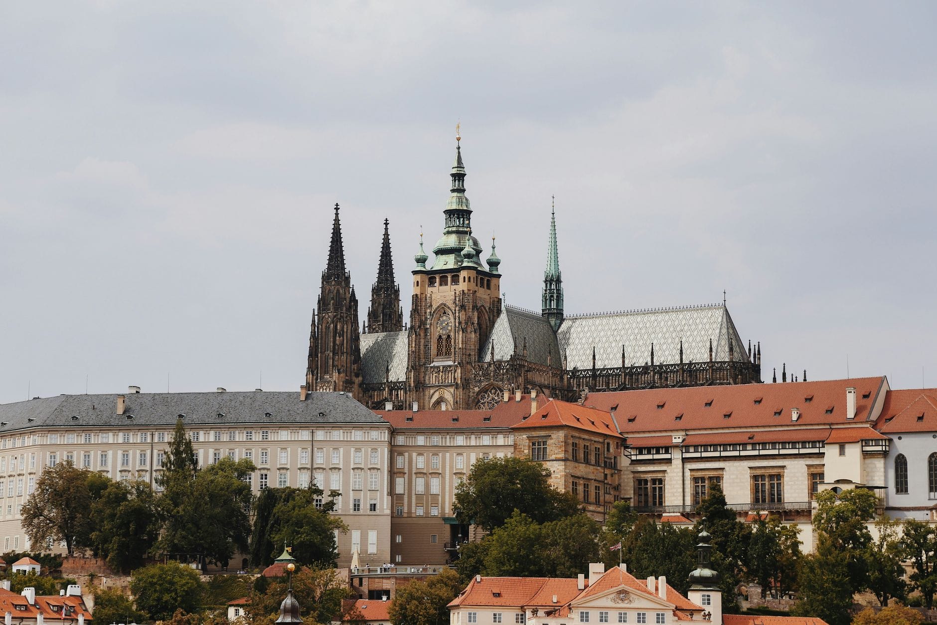 Markante Ansicht der Prager Burg mit ihren gotischen Türmen und den umliegenden historischen Gebäuden unter einem bedeckten Himmel.