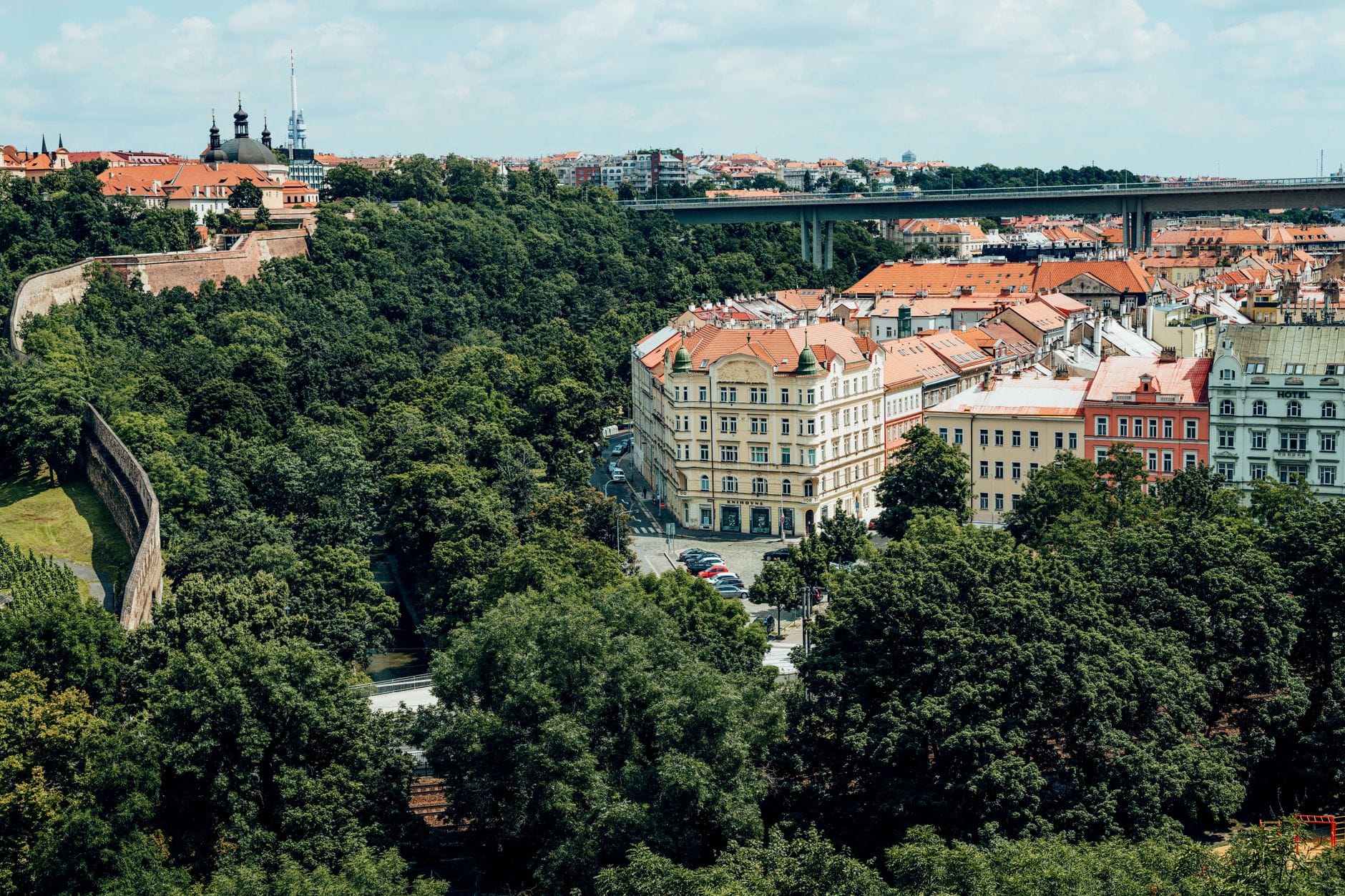 Blick auf die Festung Vyšehrad, einen üppigen Park und klassische Prager Gebäude mit einer Brücke im Hintergrund, der einen weniger besuchten Teil von Prag zeigt.