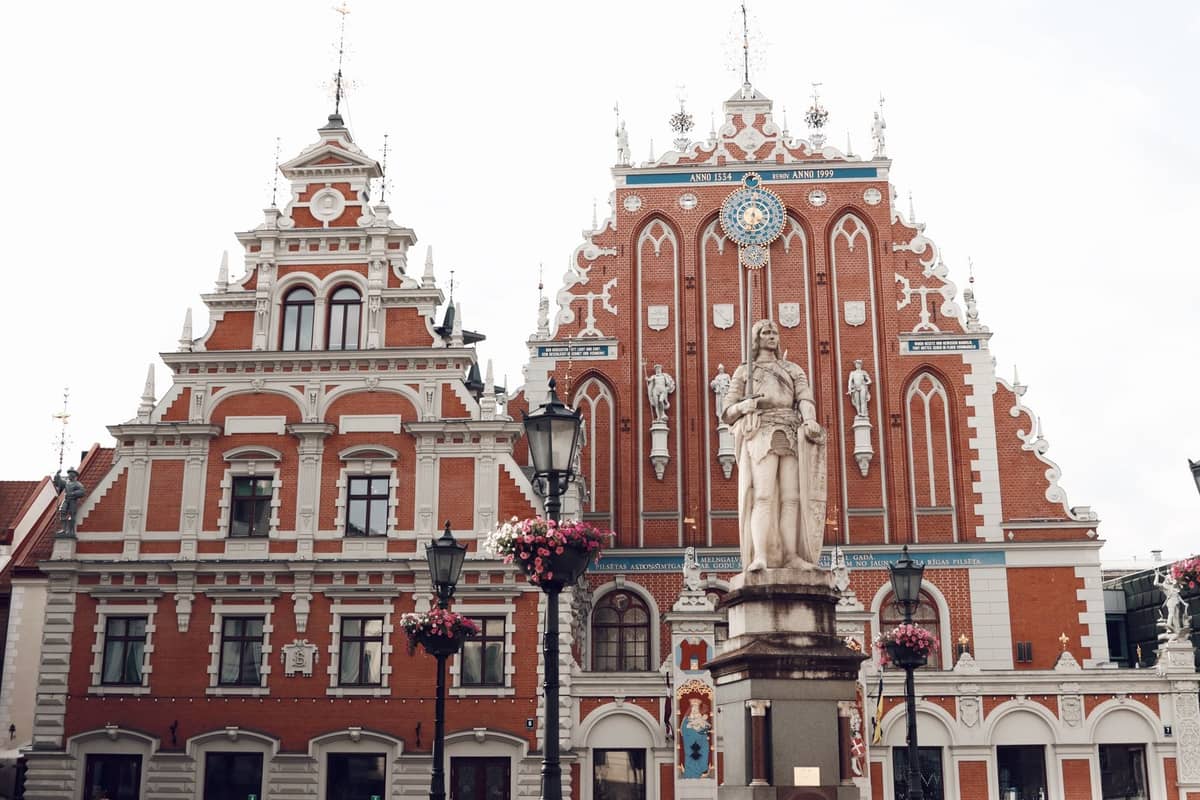 Zwei reich verzierte mittelalterliche Gebäude in der Altstadt von Riga, darunter das Schwarzhäupterhaus, mit einer Statue und dekorativen Laternen im Vordergrund.