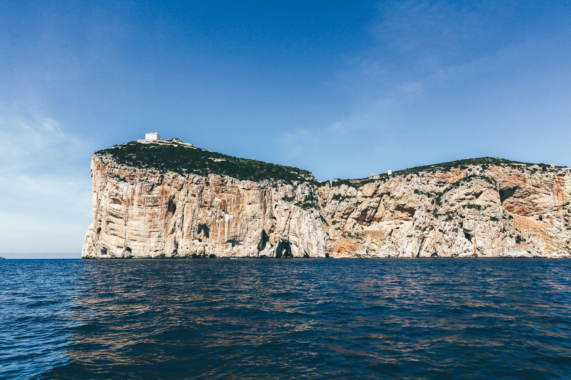 Dramatische Kalksteinklippen, die sich über das Mittelmeer erheben, mit einem Turm auf dem Gipfel und klarem blauem Himmel, in der Nähe von Alghero auf Sardinien.