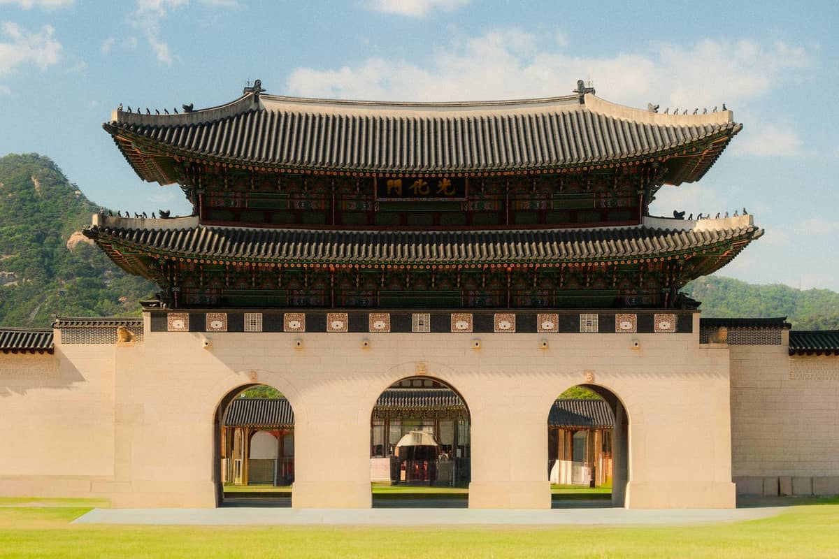 Portão principal de um grandioso palácio da era Joseon em Seul, mostrando arcos de pedra, arquitetura coreana tradicional e uma bela paisagem montanhosa ao fundo.