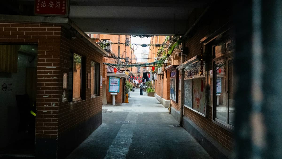 Narrow pedestrian lane with brick walls, hanging laundry, and overhead utility wires in a Shanghai shikumen neighborhood.