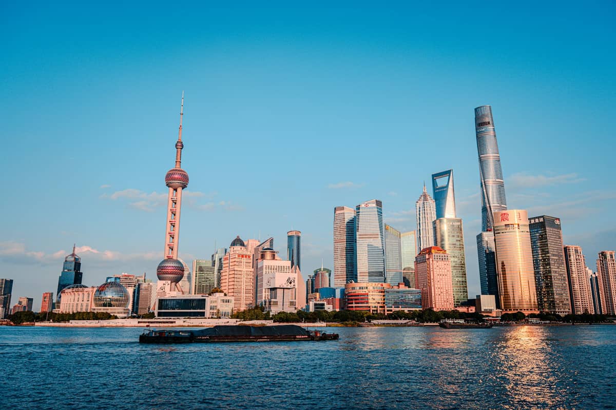 Wide view of the Pudong skyline across the Huangpu River at sunset in Shanghai, with the Oriental Pearl Tower and skyscrapers visible.