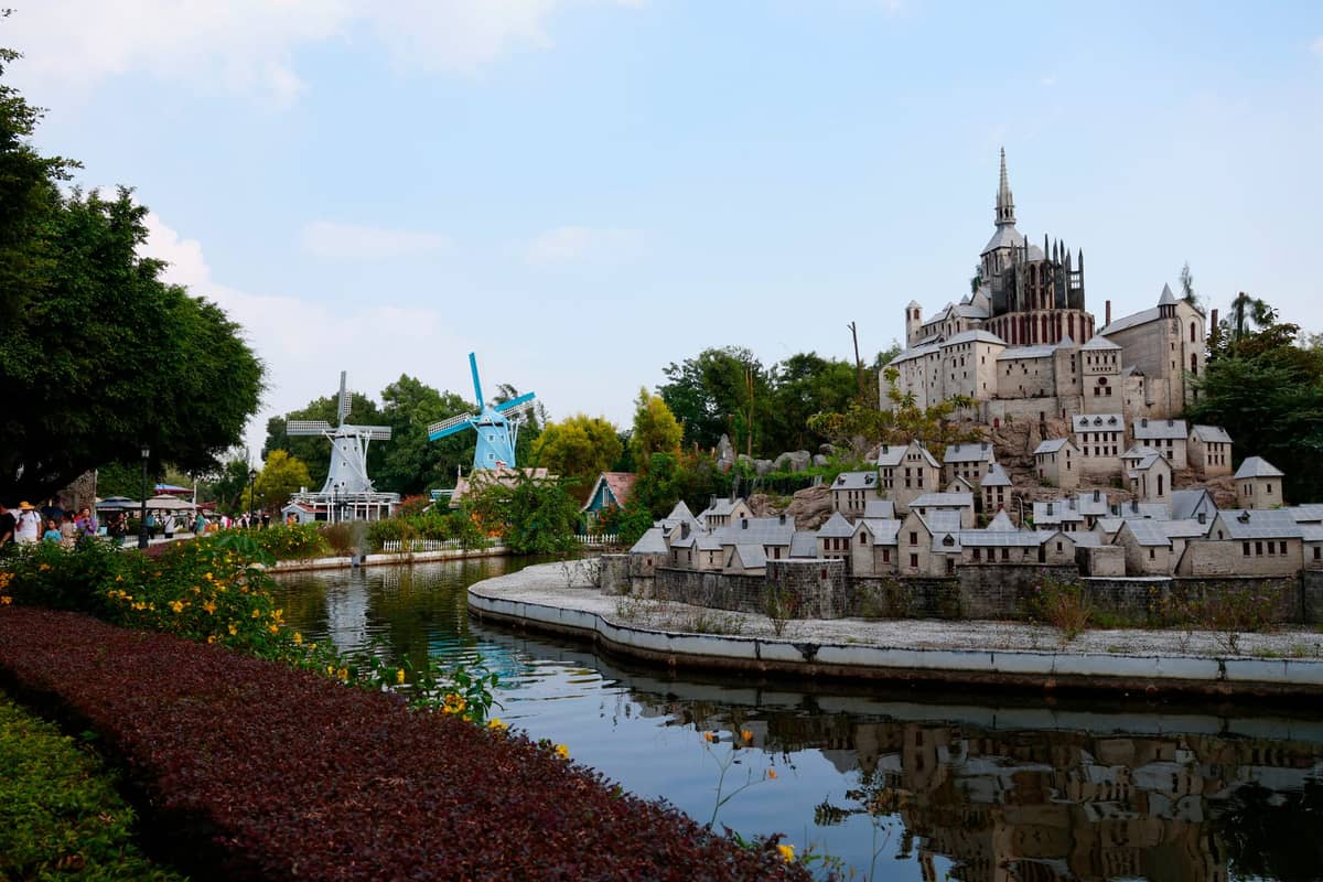 Vista de marcos europeus em escala reduzida, incluindo moinhos de vento e um castelo, em um parque em miniatura com água e árvores.