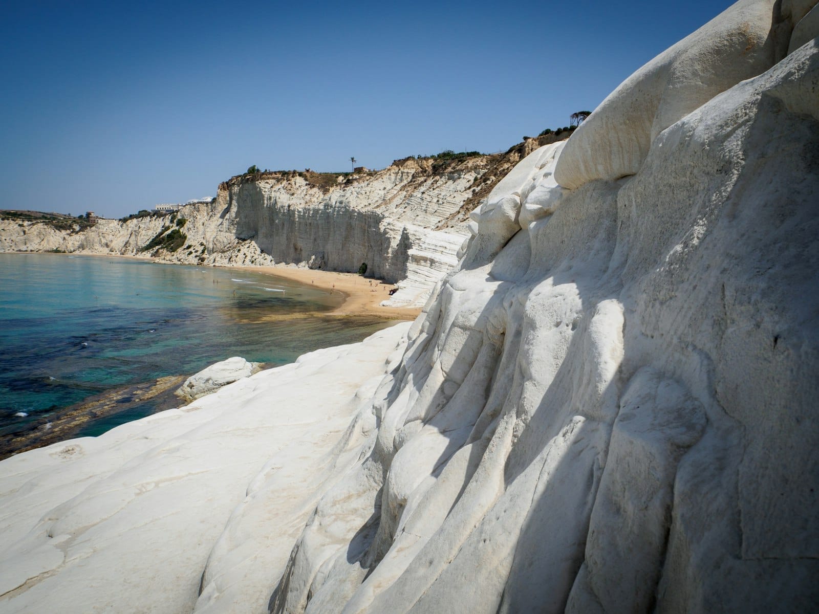 Weiße Mergelklippen der Scala dei Turchi mit klarem blauem Wasser und einem Sandstrand darunter an der sizilianischen Küste.