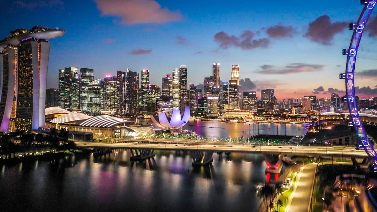 A vibrant dusk view of Singapore's Marina Bay with skyline, Marina Bay Sands, Helix Bridge, ArtScience Museum, and Singapore Flyer clearly visible.
