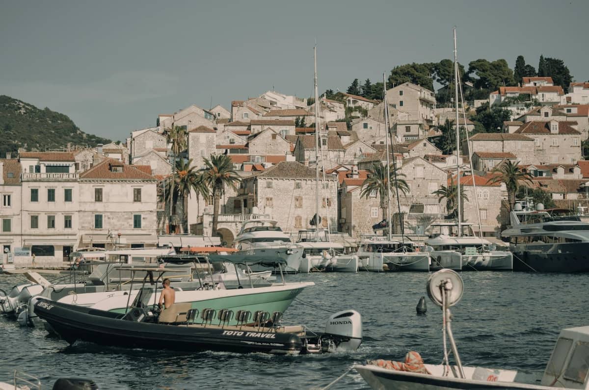 Hafenszene mit Booten auf dem Wasser, Palmen und Gebäuden der Hangstadt in Hvar in der Nähe von Split, Kroatien.