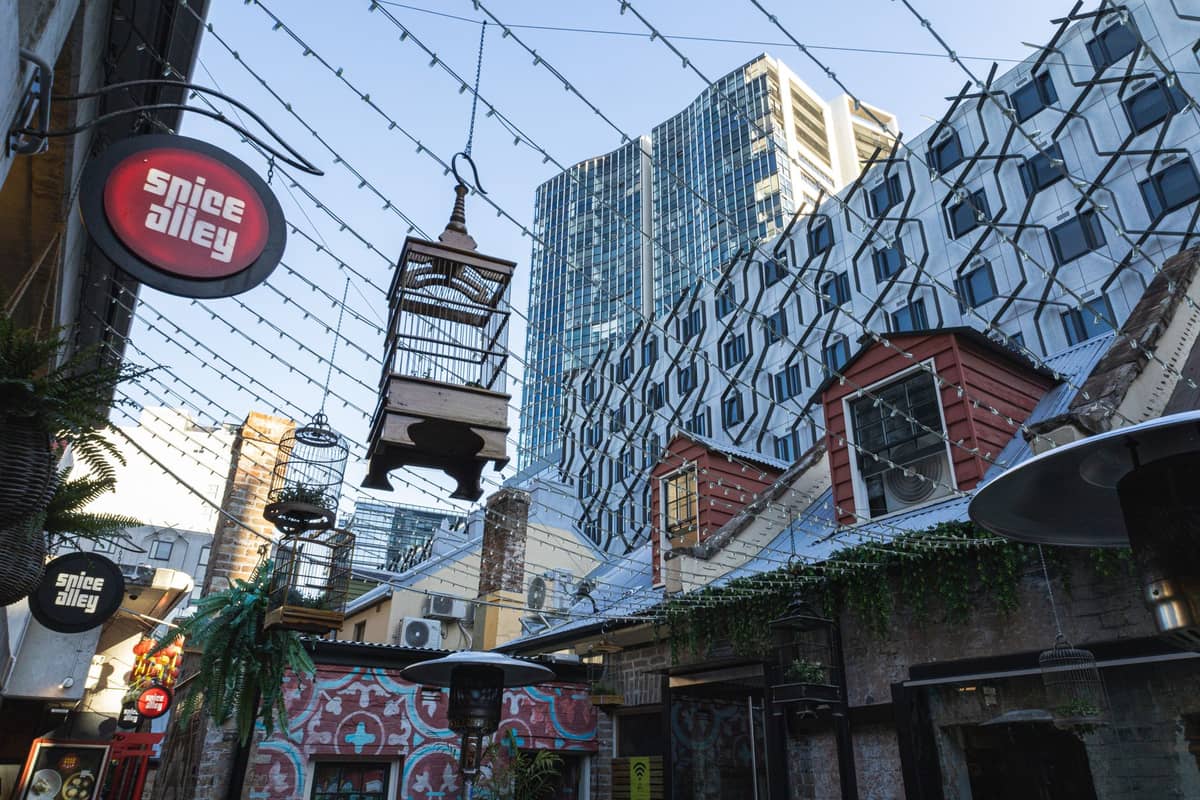 Spice Alley in Sydney, featuring street art, eclectic decorations, and distinctive architecture under string lights with modern high-rise buildings in the background.