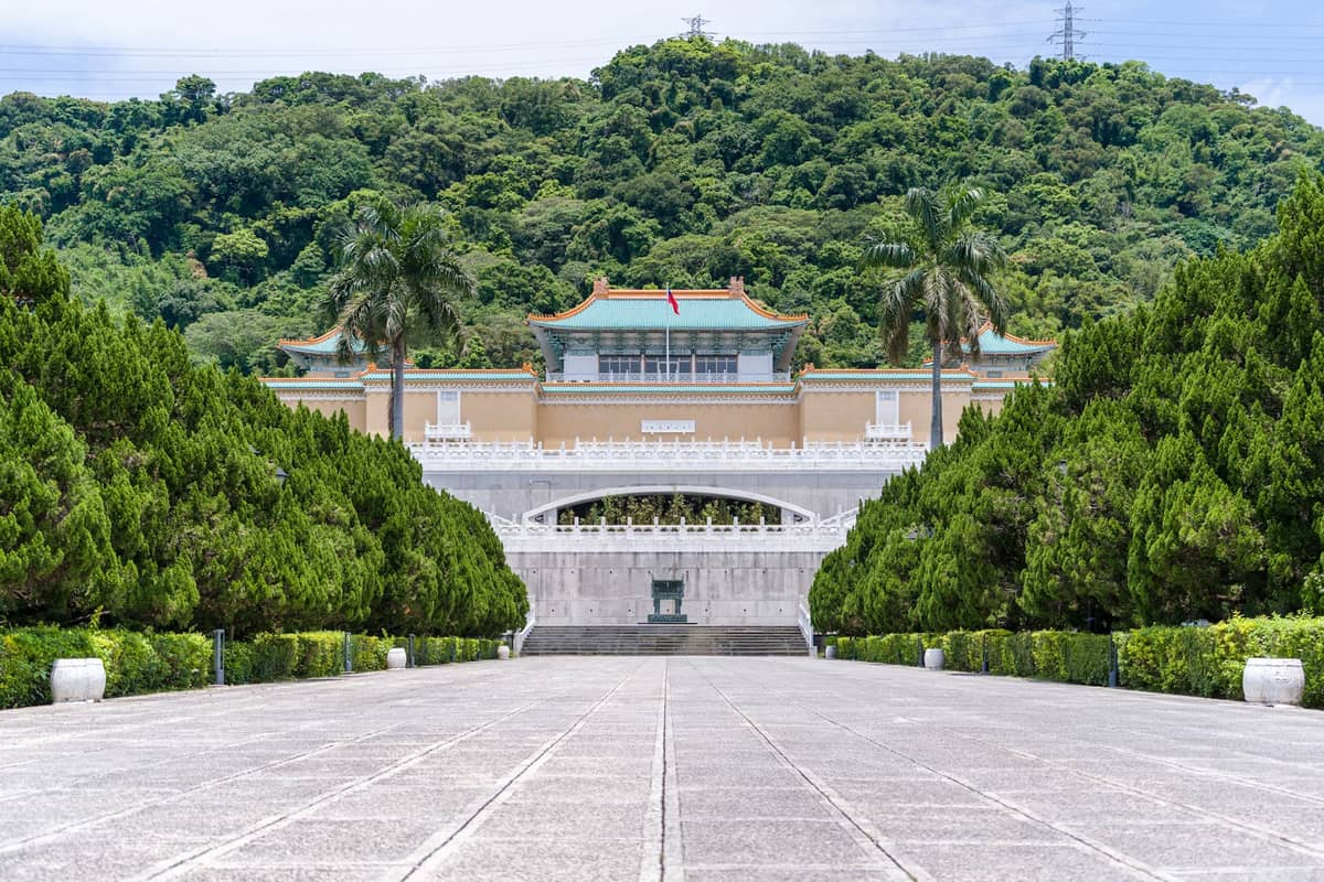 Frontansicht des National Palace Museum in Taipei, mit grünen Bäumen, einem breiten Weg und traditioneller chinesischer Architektur.