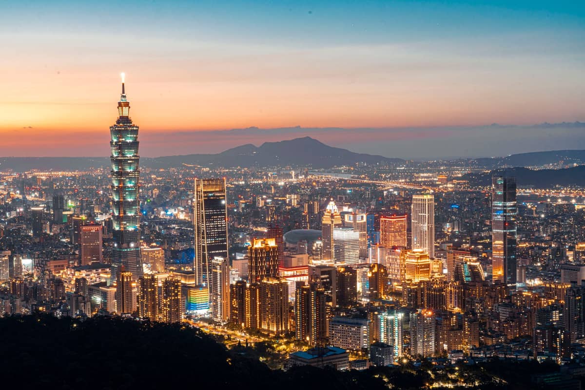 Taipeis Skyline bei Sonnenuntergang mit dem Taipei 101, der über die Stadt ragt, und beleuchtetem Stadtpanorama vor einem farbenprächtigen Himmel – aus der Vogelperspektive.