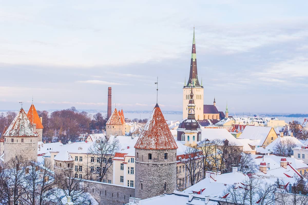 Panoramablick im Winter auf Tallinns Altstadt mit verschneiten mittelalterlichen Türmen und der Olaikirche unter einem Pastellhimmel.