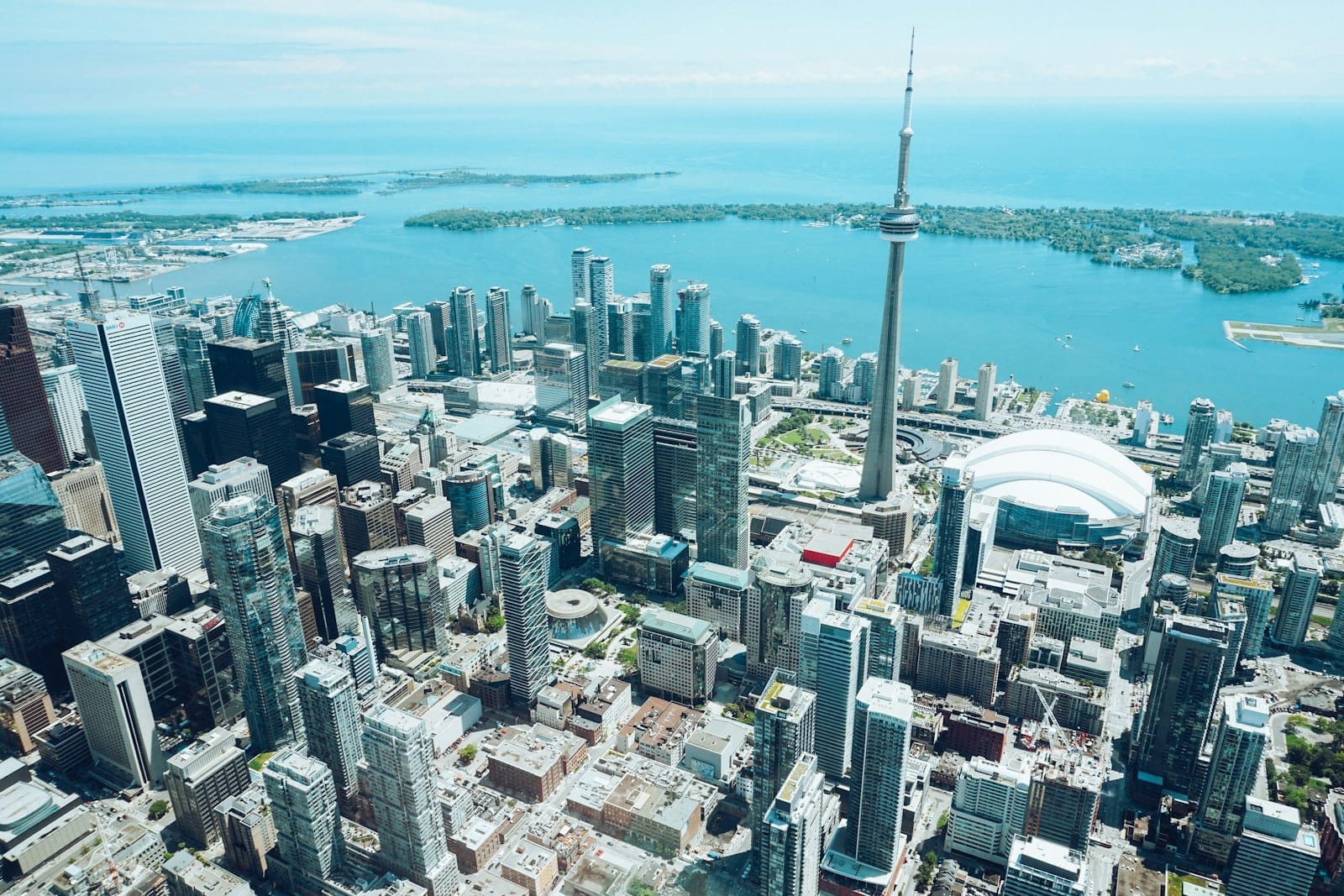Vista aérea do centro de Toronto com a CN Tower e o Rogers Centre à beira-mar em um dia claro.