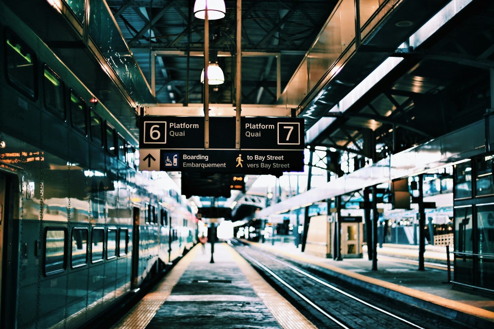 Plataformas da estação de trem de Toronto com trens da GO Transit, sinalização para as plataformas 6 e 7, e um passageiro caminhando pela plataforma.