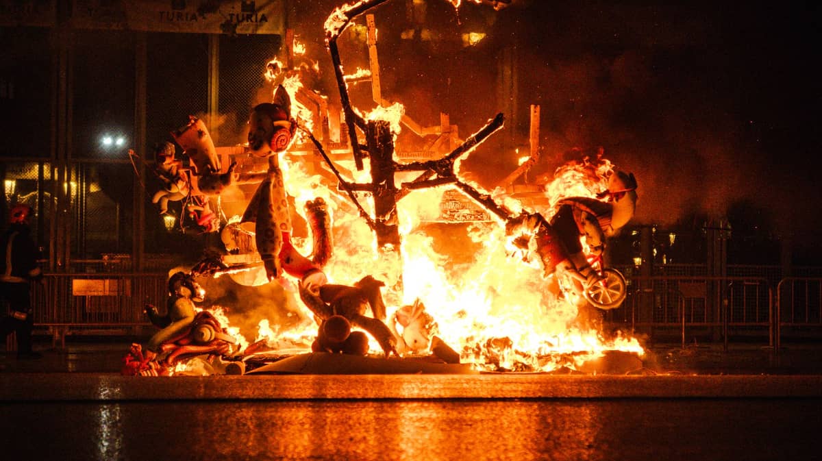 Gran monumento escultórico ardiendo intensamente durante las Fallas de noche en Valencia, multitudes al fondo