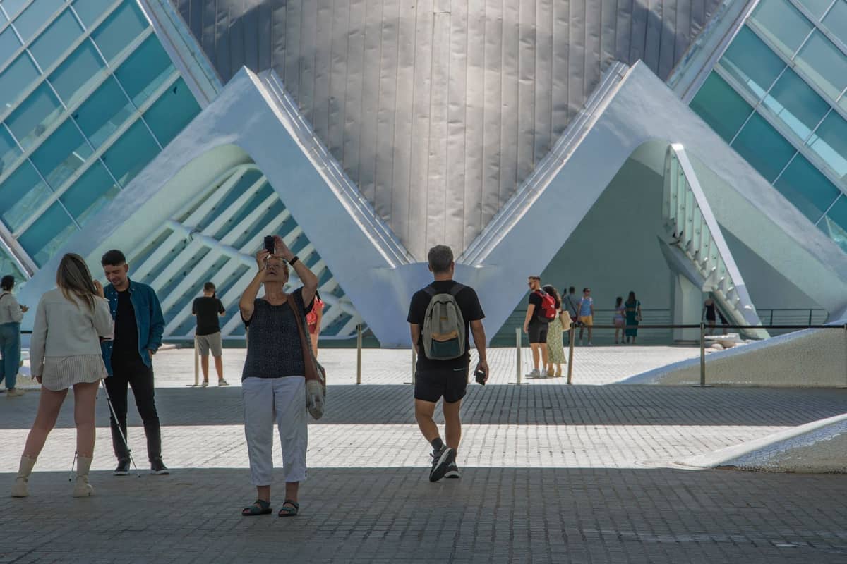 Visitatori che esplorano l'architettura futuristica della Ciudad de las Artes y las Ciencias a Valencia in una giornata di sole, con moderne strutture in vetro e acciaio in vista.